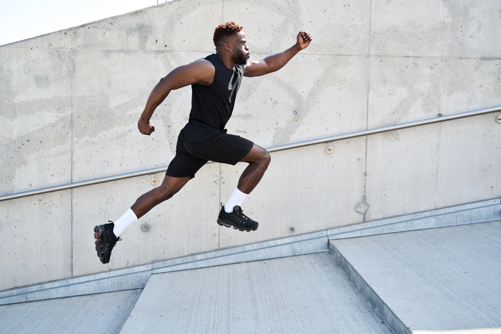 confident-strong-fit-sporty-young-black-man-running-along-urban-wall-outdoors-